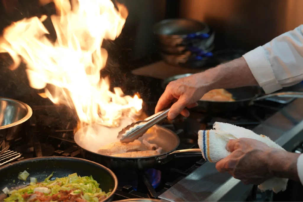 Chef grilling chicken on stove as flames leave frying pan at the purple sky winery restaurant.